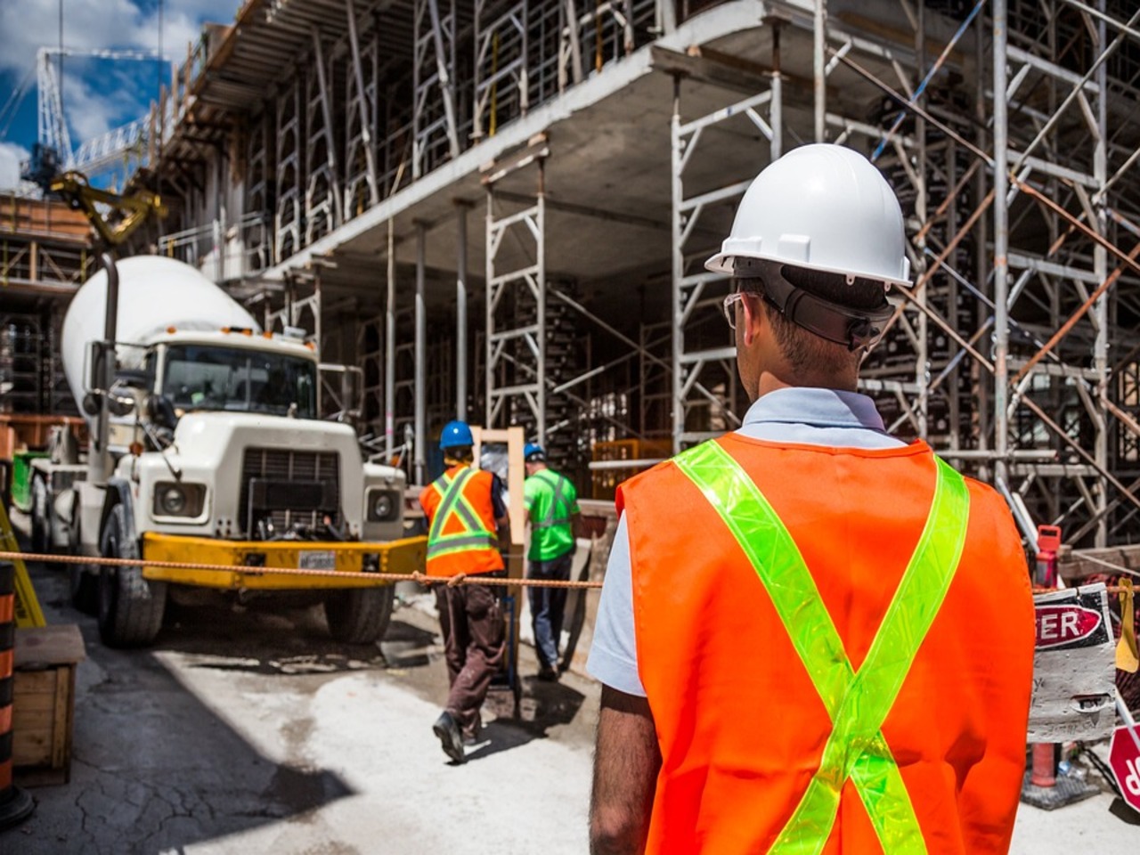 A construction worker wearing a yellow hard hat and high-visibility safety vest is focused on his work at a construction site.